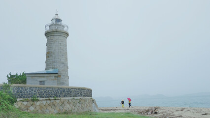 Two people heading for the lighthouse in the rain.