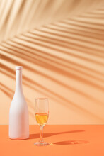 Top View Of Tropical Leaf Shadow, White Bottle And Wine Glass On Orange Background. Summer Tropical Celebration Party.