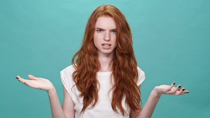 Poster - Happy ginger woman in t-shirt covering her face and disappointed after that while looking at the camera over turquoise background