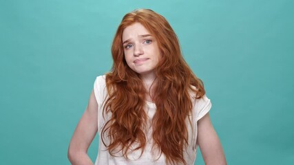 Canvas Print - Confused ginger woman in t-shirt shrugs her shoulders and looking at the camera over turquoise background