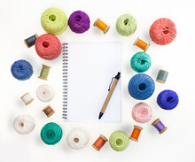 Multicolored Balls And Bobbins Of Woolen Yarn, Wooden Thread Sleeves On White Isolated Background. Notepad With Pen. Needlework, Handmade. View From Above. Isolated. Copy Space