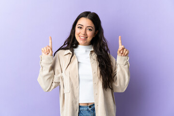 Wall Mural - young caucasian woman isolated on purple background pointing up a great idea
