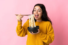 Young Caucasian Woman Isolated On Pink Background Holding A Bowl Of Noodles With Chopsticks And Eating It