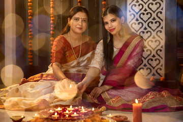 Portrait of two Indian woman lighting diyas and lamps on the festive occasion of Diwali. Celebrations at home