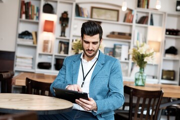 Canvas Print - Young businessman sitting at cafeteria, using tablet computer.