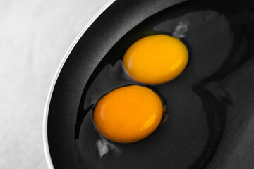 Two raw bright round yolks among transparent whites in a black frying pan. The concept of the process of cooking a simple dish for breakfast. Close-up