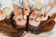 © Daria Lukoiko - Two girls make homemade face and hair beauty masks. Cucumbers for the freshness of the skin around the eyes. Women take care of youthful skin. Girlfriends laugh at home lying on the floor on pillows.