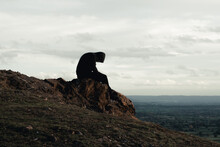 A Mental Health Concept Of A Hooded Man Sitting Alone On Top Of A Hill In The Countryside. Looking Down.