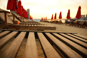 Wall Mural - wooden lounger on the beach. wooden deck chair against the background of unopened umbrellas at sunset