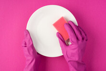 Top View Photo Of Hands In Pink Gloves Holding White Clean Dish And Pink Sponge On Isolated Pink Background