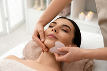 Young Woman Receiving Facial Massage With Gua Sha Tool In Beauty Salon