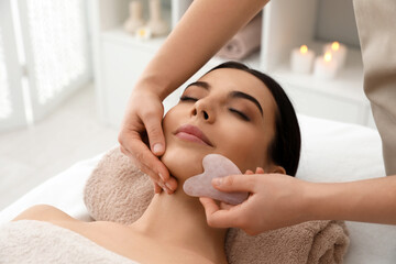 young woman receiving facial massage with gua sha tool in beauty salon