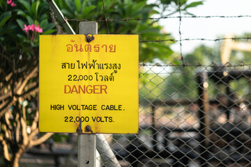 Caution sign of High voltage electricity area (Thai and English text). Industrial safety sign object photo.