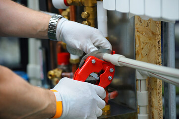 Plumber hands in gloves cut plastic pipe with the pipe cutter