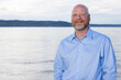 Environment portrait of bald man with a beard outside in front of ocean water. Business casual head shot wearing a button up shirt with open collar. 