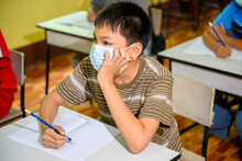 Asian Elementary School Boy Wearing A Mask To Prevent Coronavirus (COVID 19) Doing Education In A Classroom At A Rural School On The First Day Of Semester.