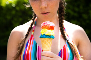 Young teenage girl eating icecream cone wearing pink sunglasses and braids on hot summer day