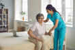 Smiling caring nurse supporting patient assisting senior woman to get up from bed helping elderly disabled lady to stand up. Old people recovery, rehabilitation and care professional service