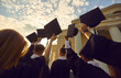 © Studio Romantic - Graduation ceremony event celebration. Diverse student wearing gown mantles standing in group holding raised hat rear view from bottom. Shot over sunset and university high school building