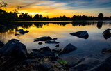 Fototapeta Pomosty - Sonnenuntergang am See mit Steinen im Vordergrund