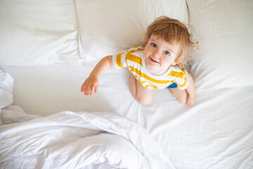 Top view of cheerful little boy in white bed early in the morning. Portrait of a handsome boy awakened