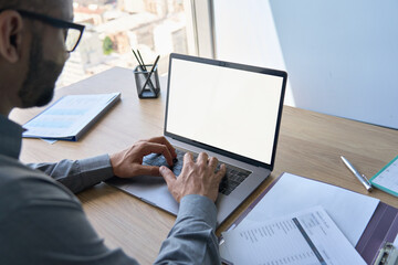 Over shoulder closeup view of male indian businessman wearing glasses looking at empty blank mockup screen for advertising, working, typing, planning, analyzing data. Business technologies concept.