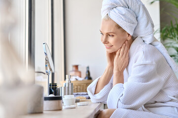 attractive mid age older adult 50 years old blonde woman wears bathrobe and towel in bathroom touchi