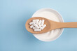 Capsules probiotic on a wooden spoon and bowl with homemade yogurt on light blue background. Fermented foods, dairy, nutritional supplement, healthy digestion concept. Top view, flat lay