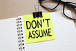 Don't Assume. sticker attached to a notebook on aa wood background near beautiful glasses