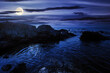 sea coast scenery at night. boulders in the calm water. few clouds on the sky in full moon light. lonely place for summer vacations. sunny weather
