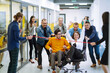 © maxbelchenko - Young colleagues group having fun together, riding on chairs in office, diverse excited office workers enjoying break, laughing, engaged funny activity, celebrating corporate success.