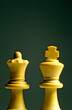 Vertical shot of white king and queen chess pieces on a green background