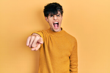 Poster - handsome hipster young man wearing casual yellow sweater pointing displeased and frustrated to the c