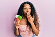 © Krakenimages.com - Young latin woman holding ice cream covering mouth with hand, shocked and afraid for mistake. surprised expression