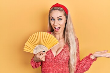 Sticker - Young caucasian woman waving hand fan cooling air in summer celebrating achievement with happy smile and winner expression with raised hand