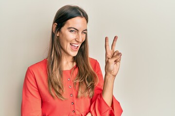 Young beautiful woman wearing casual clothes smiling with happy face winking at the camera doing victory sign. number two.