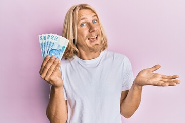 Sticker - Caucasian young man with long hair holding 50 polish zloty banknotes celebrating achievement with happy smile and winner expression with raised hand