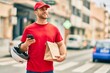 © Krakenimages.com - Young caucasian deliveryman using smartphone and holding delivery paper bag at the city.