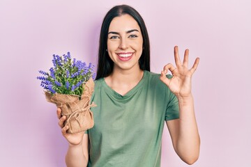 Sticker - Beautiful woman with blue eyes holding lavender plant doing ok sign with fingers, smiling friendly gesturing excellent symbol