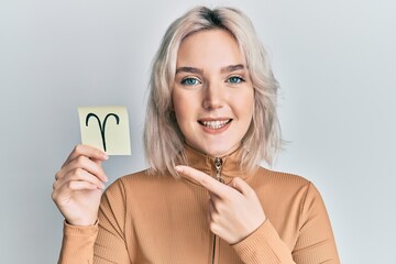 Sticker - Young blonde girl holding paper with aries zodiac sign smiling happy pointing with hand and finger