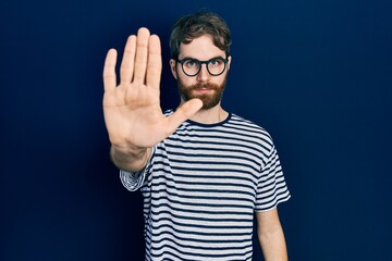 Wall Mural - caucasian man with beard wearing striped t shirt and glasses doing stop sing with palm of the hand. 