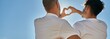© Krakenimages.com - Young gay couple on back view doing heart symbol with hands at the beach.