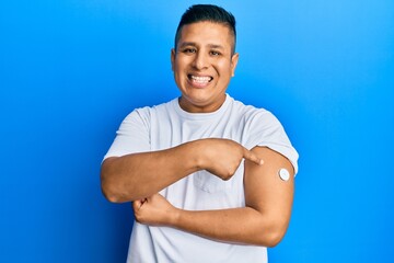 Canvas Print - Young latin man using glucose meter button on arm smiling with a happy and cool smile on face. showing teeth.