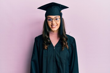 Young hispanic woman wearing graduation cap and ceremony robe with a happy and cool smile on face. lucky person.