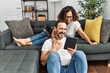© Krakenimages.com - Middle age hispanic couple smiling happy and using touchpad. Sitting on the sofa with dogs at home.
