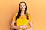 Fototapeta  - Young hispanic woman wearing student backpack and holding book looking at the camera blowing a kiss being lovely and sexy. love expression.