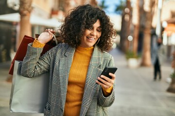 Young hispanic woman going shopping and using smatphone at the city.