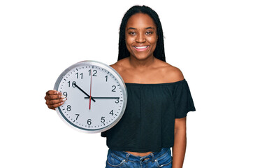 Poster - Young african american woman holding big clock looking positive and happy standing and smiling with a confident smile showing teeth