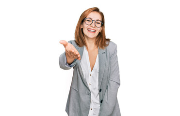 Poster - Young caucasian woman wearing business style and glasses smiling friendly offering handshake as greeting and welcoming. successful business.