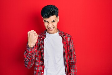 Wall Mural - Young hispanic man wearing casual clothes angry and mad raising fist frustrated and furious while shouting with anger. rage and aggressive concept.